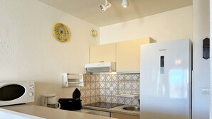 Uma cozinha compacta com micro-ondas, fogão, geladeira e um relógio amarelo na parede.