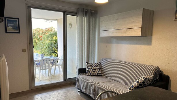 Een kamer met een bank, een tafel en uitzicht op een buitenruimte met stoelen en groen.