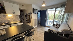 Een moderne keuken met een donker aanrecht, barkrukken en uitzicht op de woonkamer met een bank en gekleurde kussens.