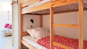 Ein Stockbett mit Holzrahmen und einer roten Bettdecke mit Muster.