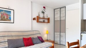 Ein Wohnzimmer mit einem gestreiften Sofa, einem Holzstuhl, einem Tisch mit Blumenmuster und einer Lampe. An der Wand hängt ein Gemälde.