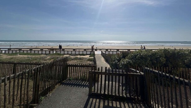 Ein Strandweg führt zum Ufer, begleitet von einem Holzzaun und mit freiem Blick auf das Meer.