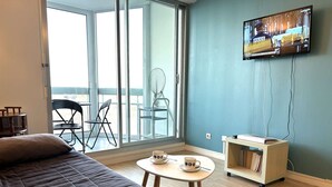 Ein Zimmer mit einem Bett, einem kleinen Tisch mit zwei Tassen, einem Fernseher an der Wand und Blick durch eine Schiebetür.