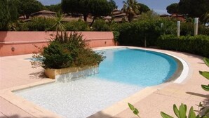 A swimming pool with a curved edge, surrounded by a low wall and greenery. - Sunny 2-Room Apartment with Terrace and Pool, Near Beach (Le Lavandou)
