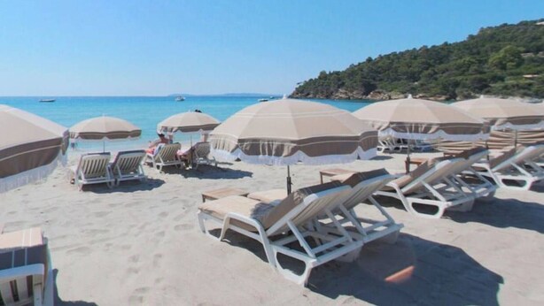 A beach with sun loungers and umbrellas, a clear sky, and a hilly landscape in the background. - Sunny 2-Room Apartment with Terrace and Pool, Near Beach (Le Lavandou)