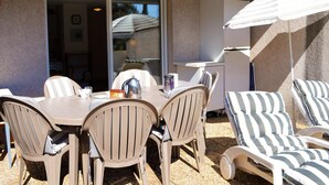 An outdoor patio with a table and chairs, a grill, and striped lounge chairs. - Sunny 2-Room Apartment with Terrace and Pool, Near Beach (Le Lavandou)