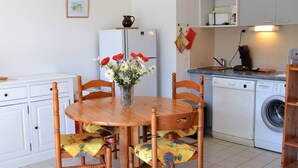 A compact kitchen with a dining table, chairs, a refrigerator, a washing machine, and a small cabinet. - Sunny 2-Room Apartment with Terrace and Pool, Near Beach (Le Lavandou)