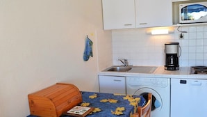Una cocina compacta con lavadora, cafetera y un aparador de madera.