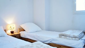 Una habitación sencilla y limpia con dos camas individuales, una mesita de noche con lámpara y una ventana.