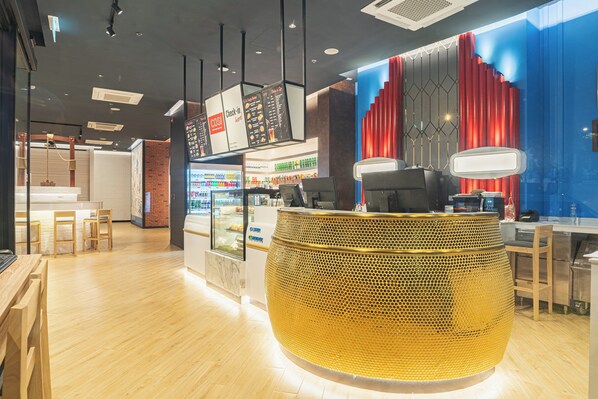 Un interior moderno con una recepción central, una vitrina de alimentos y una zona de estar con sillas de madera.