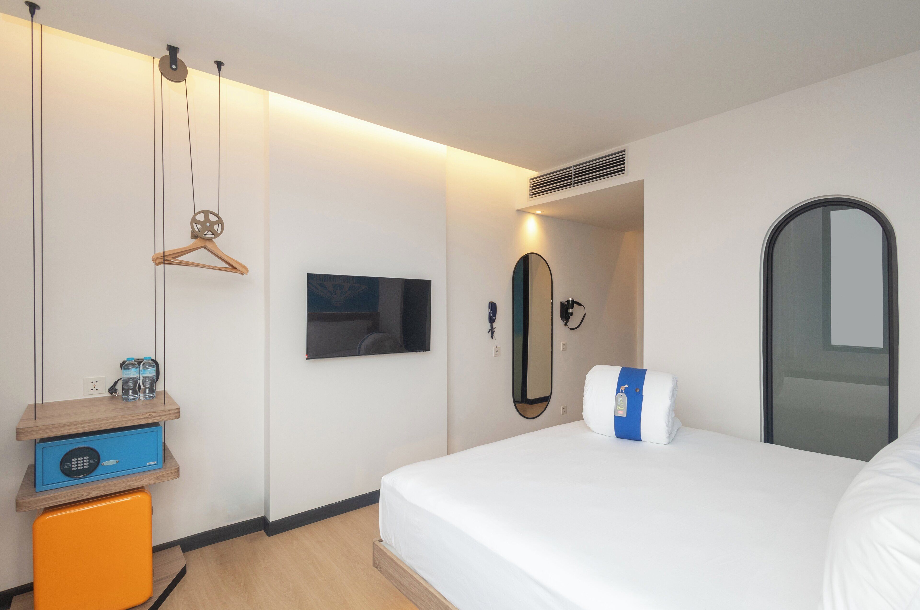 A hotel room with a bed, a TV, a mirror, a wardrobe, and a small orange cabinet.