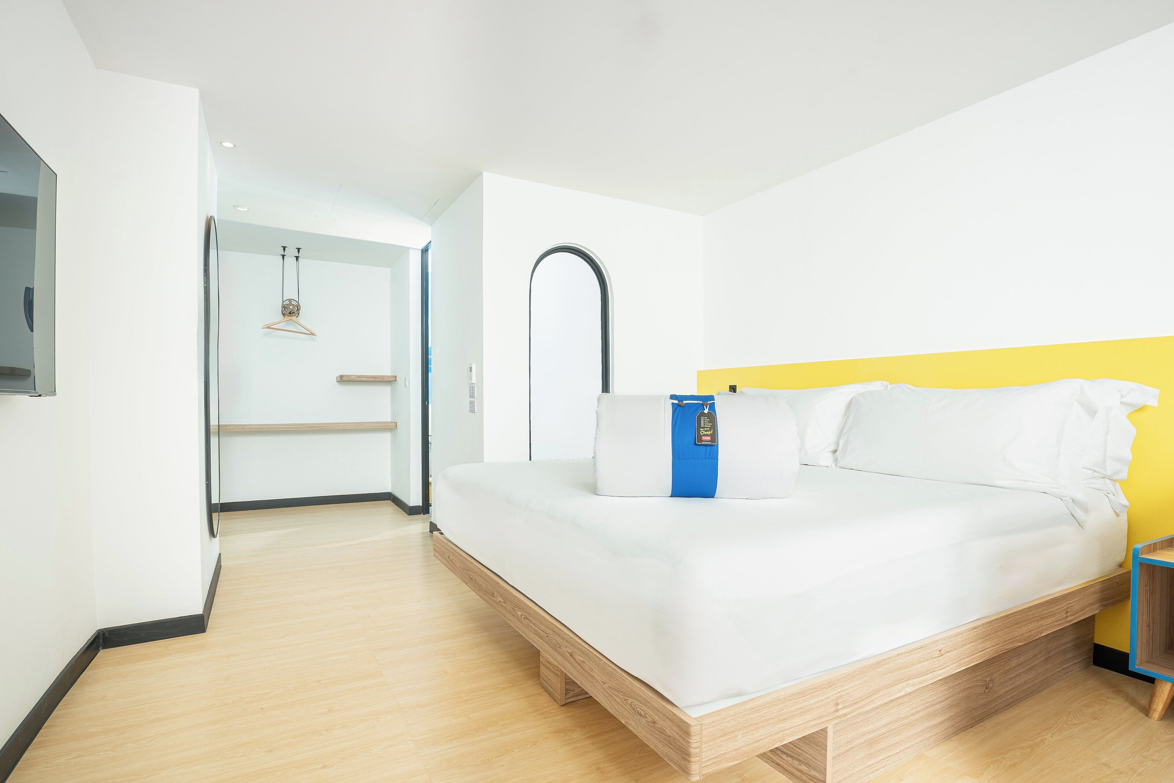 Camera d'albergo moderna con struttura letto in legno, biancheria da letto bianca e una parete gialla.