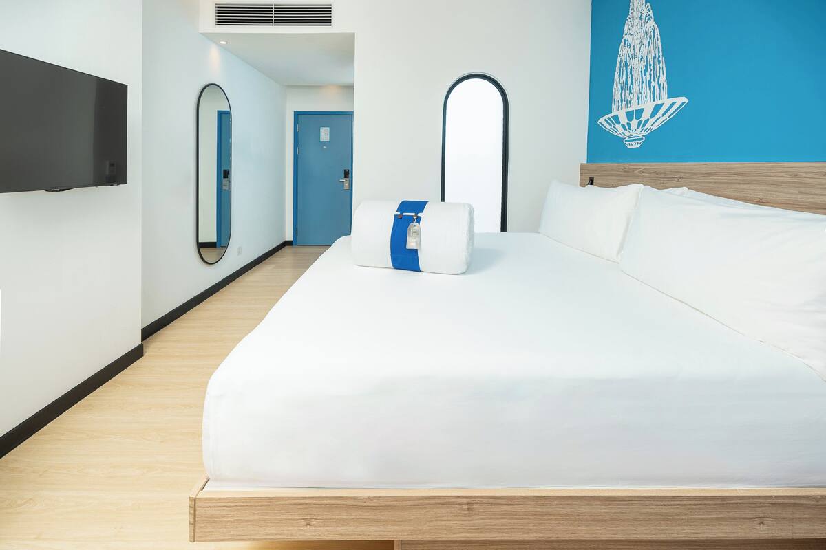 Een moderne hotelkamer met een bed, een flatscreen televisie aan de muur, een blauwe deur en een decoratief object aan de wand.