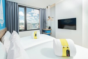 Una habitación de hotel con cama, mesita de noche con lámpara, televisor en la pared y ventana con cortinas.