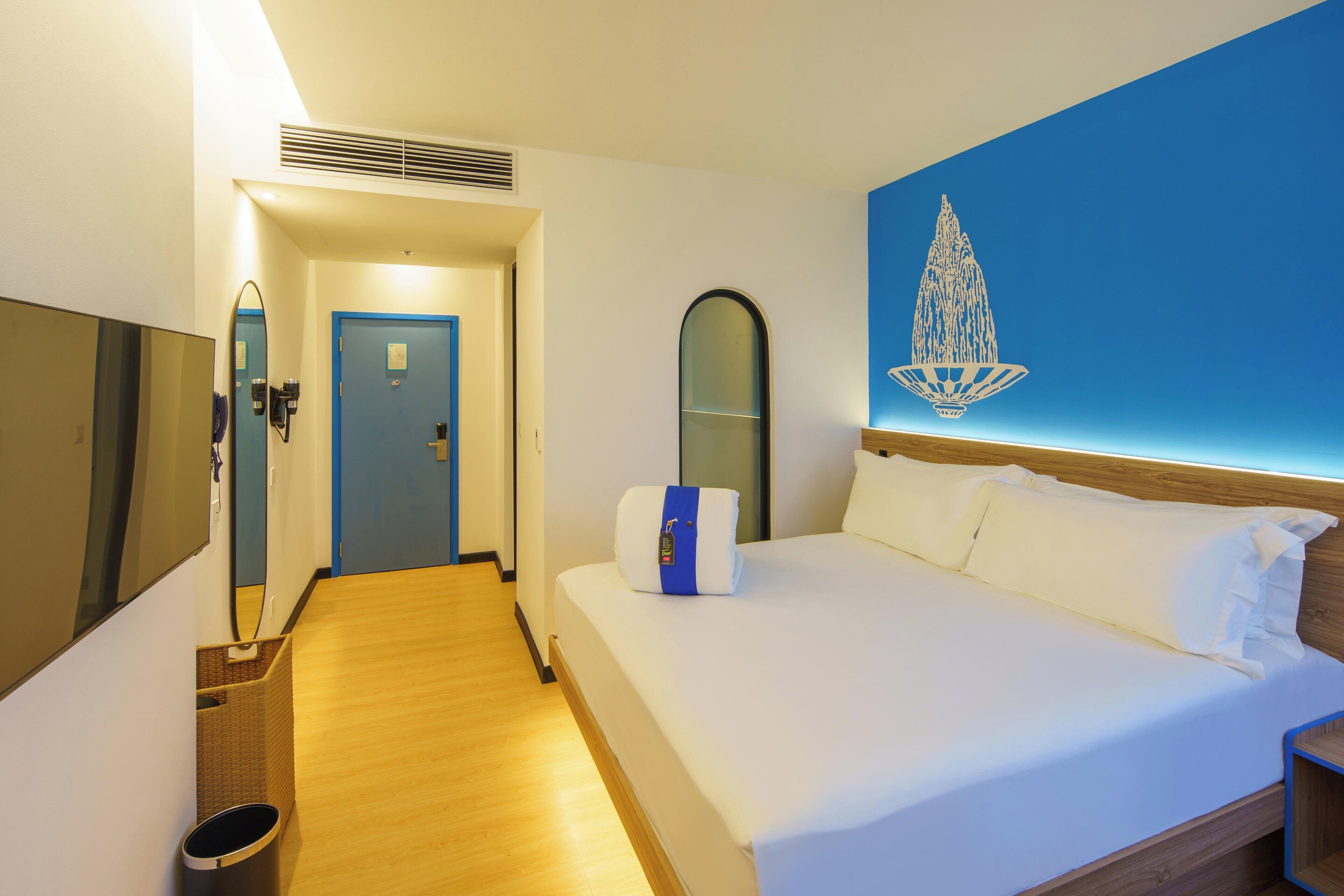Habitación de hotel con cama, suelo de madera, puerta azul, espejo adosado a la pared y decoración en la pared.