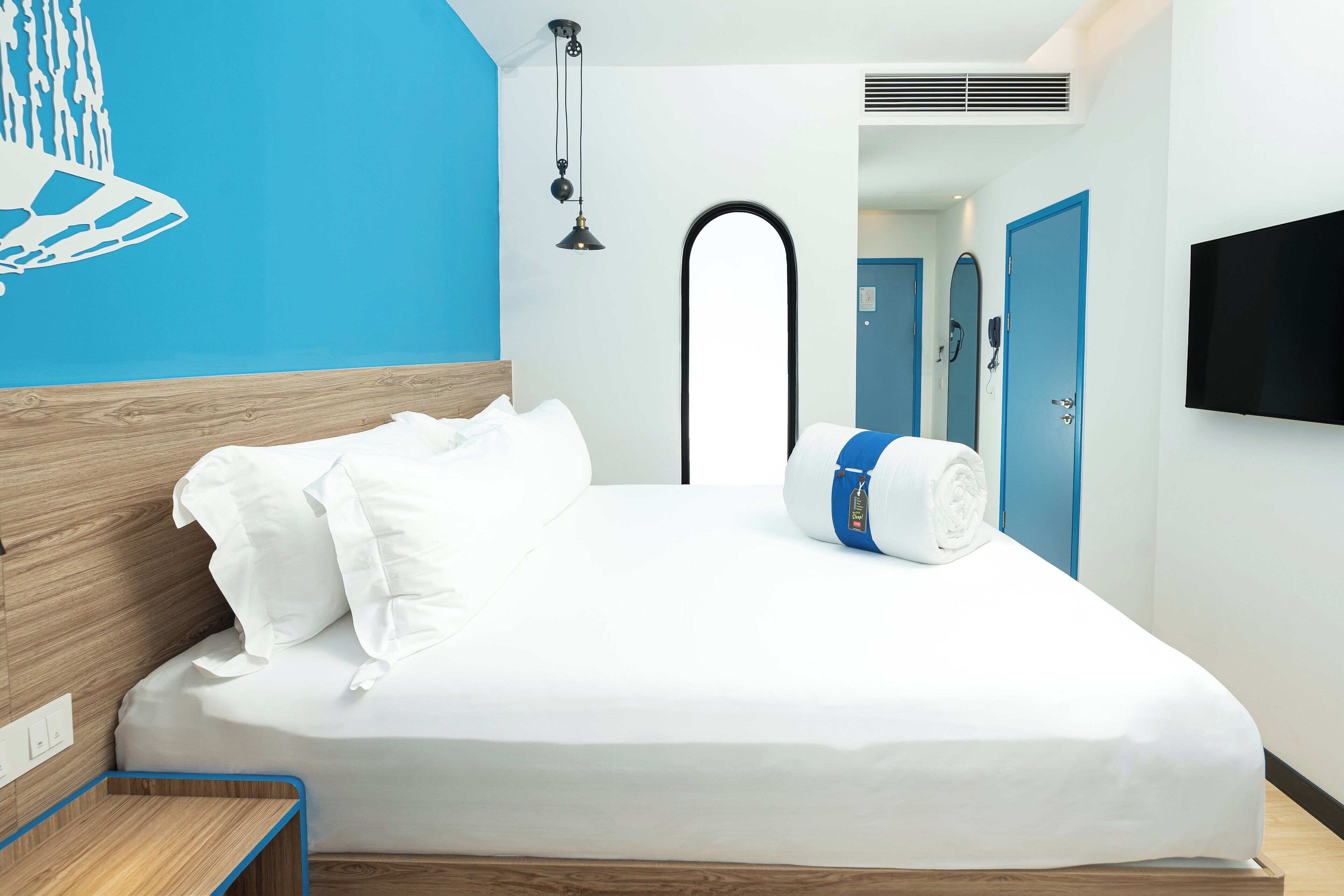 Ein modernes Hotelzimmer mit einem aufgereihten Bett, einem Holz-Kopfschild, einer blauen Akzentwand, einem Flachbildfernseher und einem Wandheizkörper.