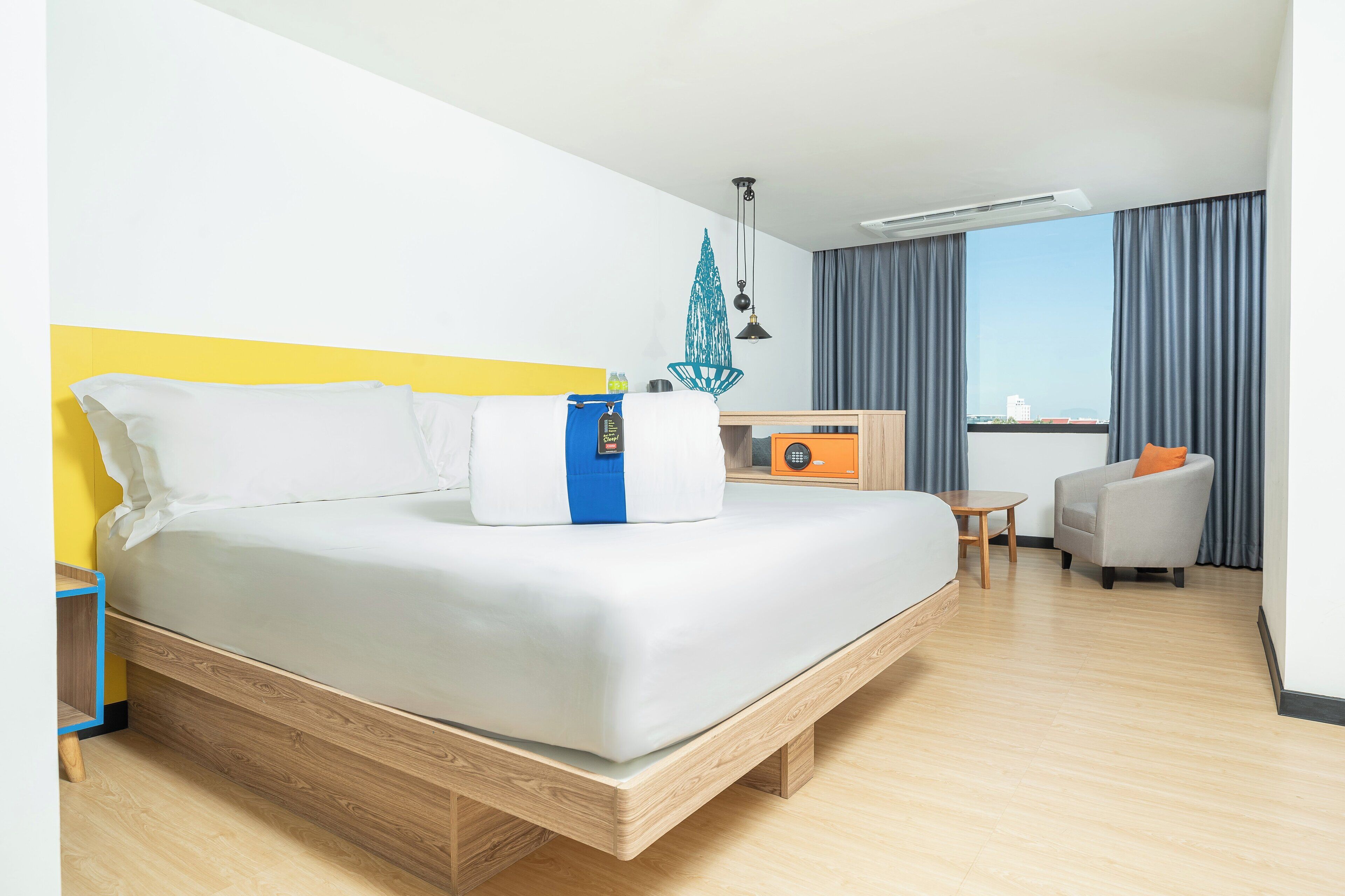 A modern hotel room with a large bed, a small desk, a chair, and a view of the city through the window.