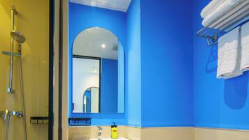 Une salle de bain équipée d’une douche, d’un lavabo et de toilettes, avec un mur bleu et un grand miroir.