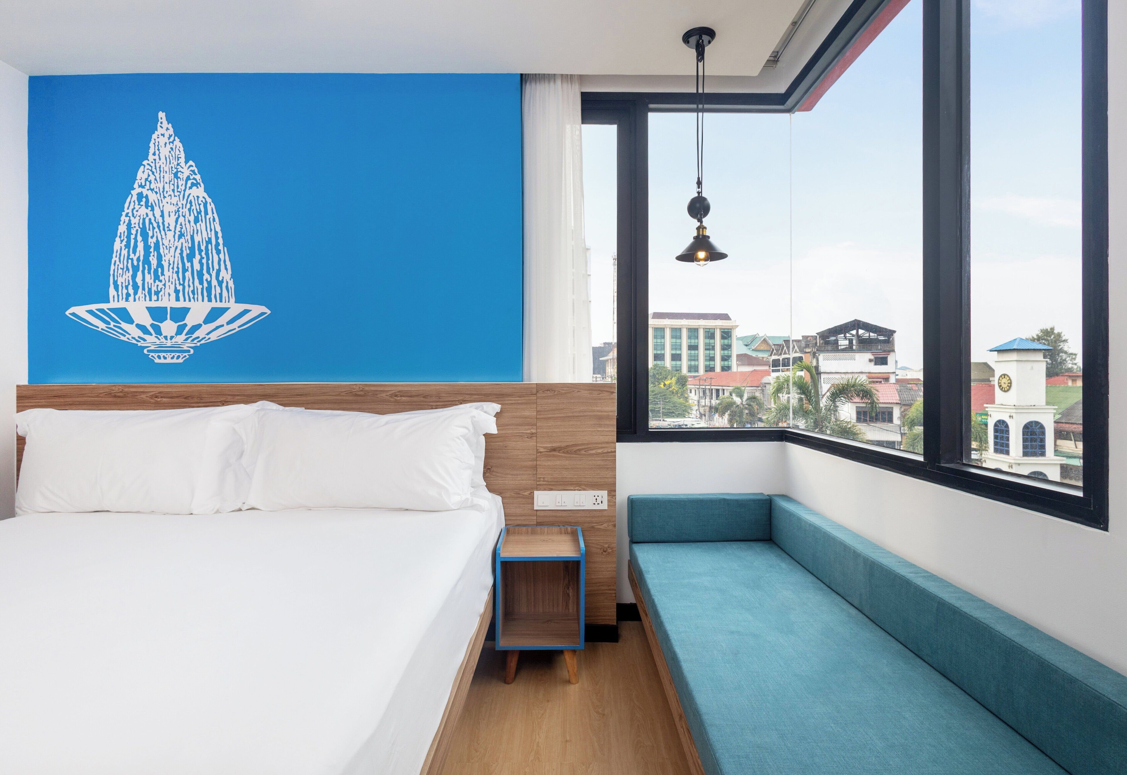 A hotel room with a large bed, a blue accent wall, a view of the city, and a small seating area by the window.