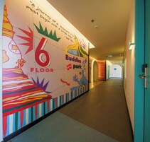 A hallway with a colorful mural on the wall, a sign indicating the 6th floor, and a Buddha park illustration.