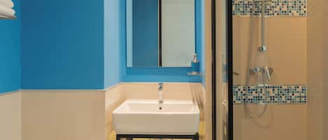 Ein Badezimmer mit einem weißen Waschbecken, blauen Wänden, einer Duschkabine aus Glas und einem Spiegel über dem Waschbecken.