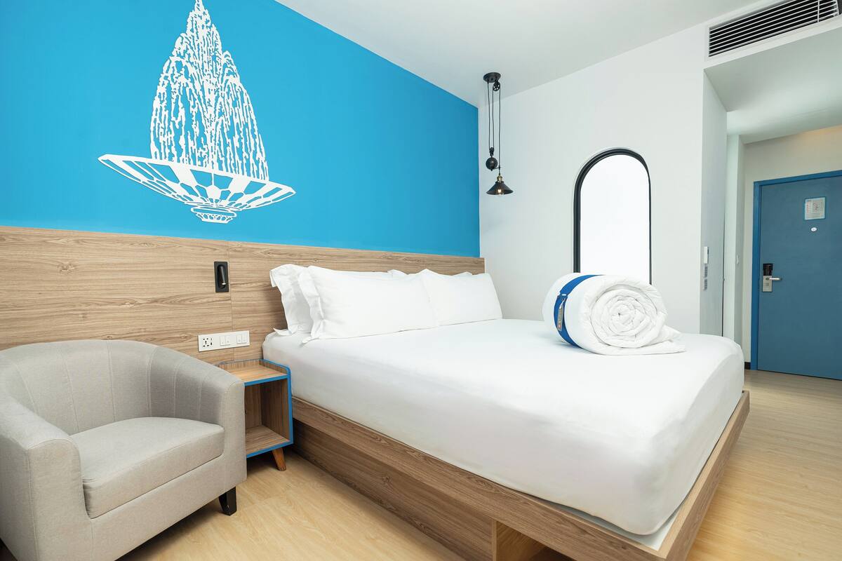 Een moderne hotelkamer met een bed, een stoel, een blauwe muur met een witte decoratieve versiering, en een deur.