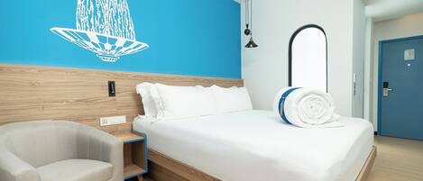 A modern hotel room with a bed, a chair, a blue wall with a white decorative element, and a door.