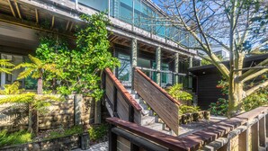 Un edificio moderno con terraza de madera, escalera y abundante vegetación.