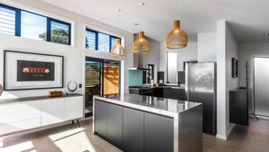 Una cocina moderna con una isla central, luces colgantes y un ventanal grande.