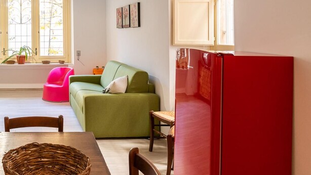 A living room with a green sofa, a red refrigerator, and a dining table with a wicker basket. - Casa Mameli by Wonderful Italy (Conversano)