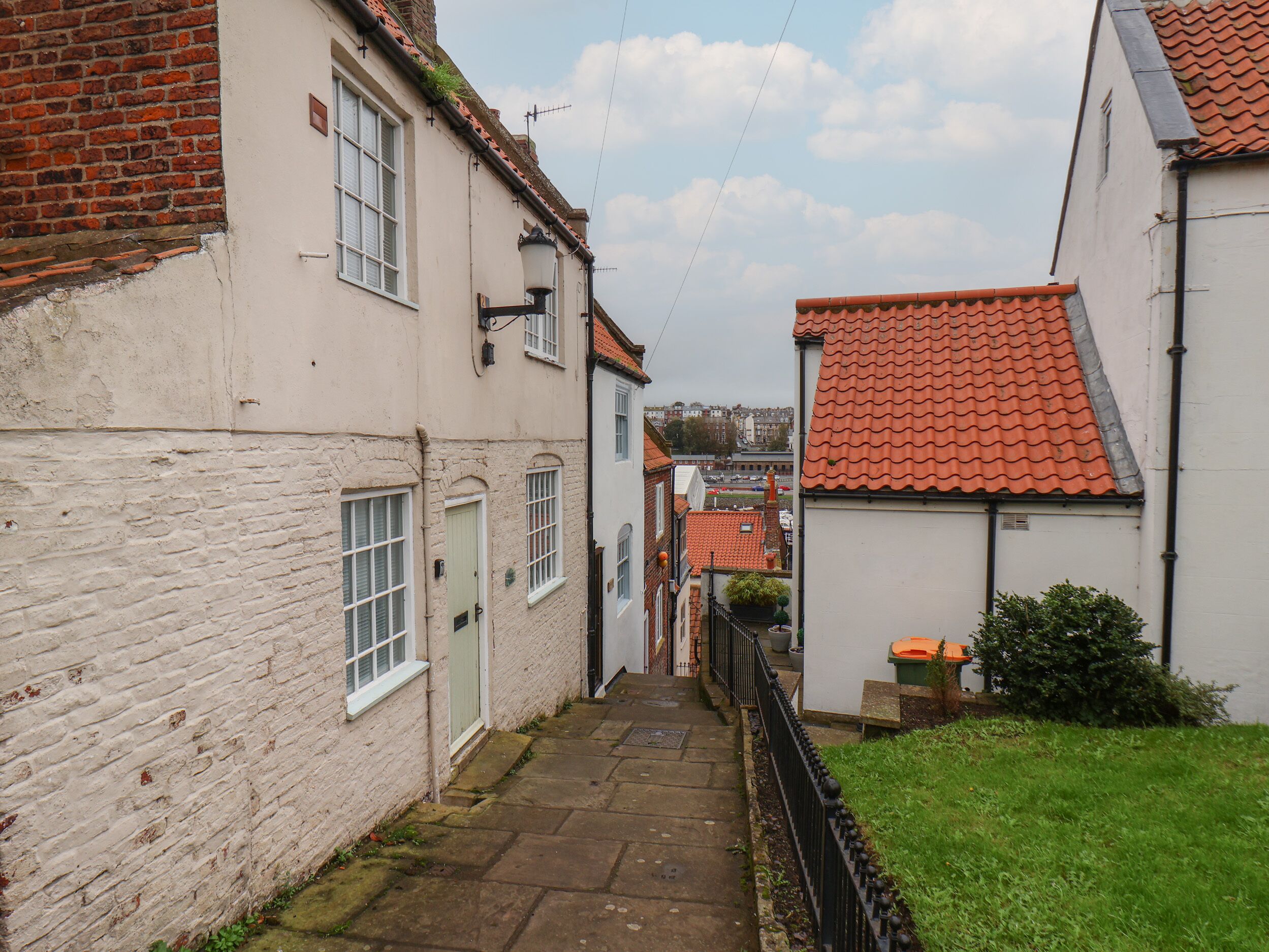 A narrow alleyway between buildings with a brick wall on one side and a white building with a red-tiled roof on the other.