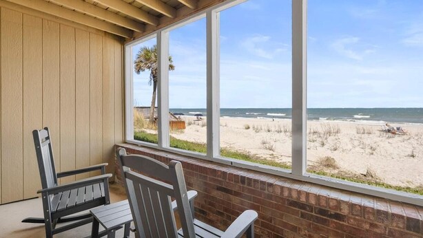 A room with a view of the beach, two wooden chairs, and a brick wall. - Oceanfront Studio with Private Porch 1st Floor (Pawleys Island)