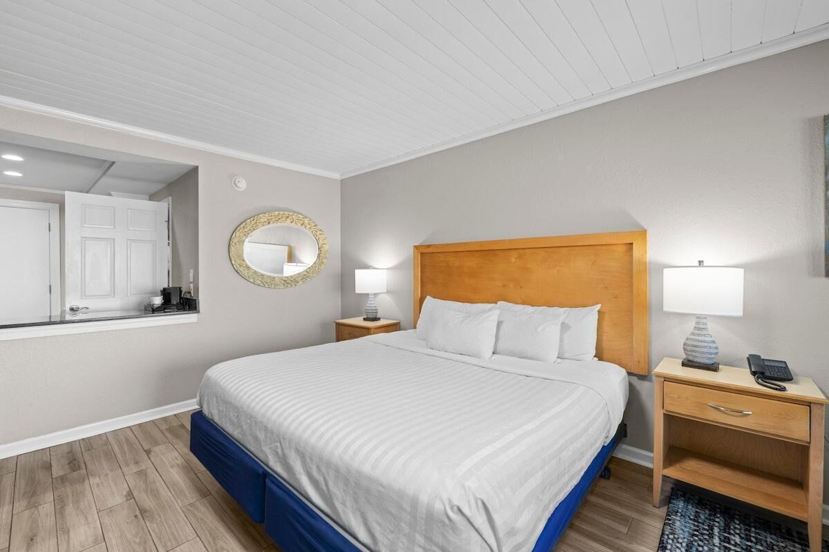 Una habitación de hotel con una cama, dos mesitas de noche, un espejo y una ventana.