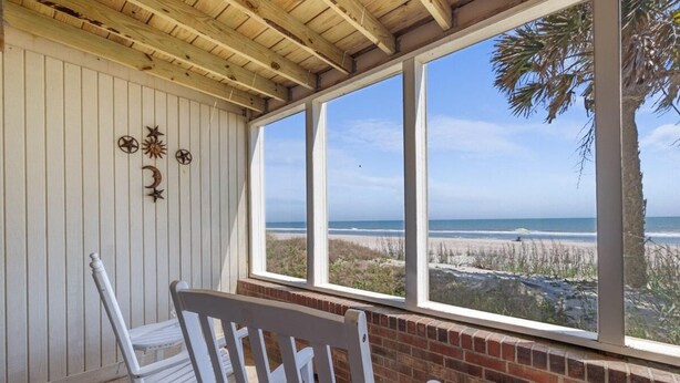 A covered patio with a view of the beach, white chairs, and decorative wall elements. - Coastal Getaway in our Oceanfront Dune Room (Pawleys Island)