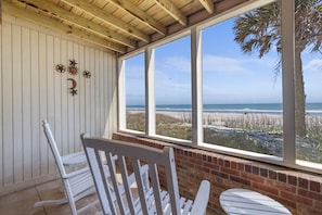 A covered patio with a view of the beach, white chairs, and decorative wall elements.