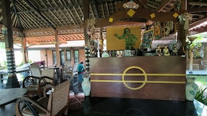 Un espace extérieur abrité, aménagé avec des tables et des chaises, et décoré d’objets d’art et de masques reflétant la culture locale.