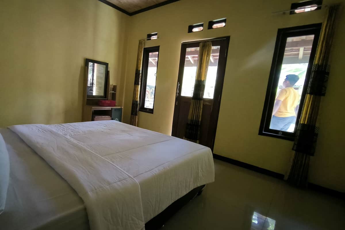 Ein Hotelzimmer mit Bett, Spiegel, kleinem Schreibtisch und einem Fenster mit Vorhängen.