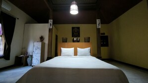 Une chambre d’hôtel avec un grand lit, une tête de lit en bois, une statue de Bouddha fixée au mur et un luminaire au plafond.