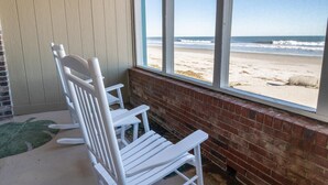 A beach view from a room with white rocking chairs and a brick wall. - Ultimate Coastal Getaway Oceanfront Dune Room (Pawleys Island)
