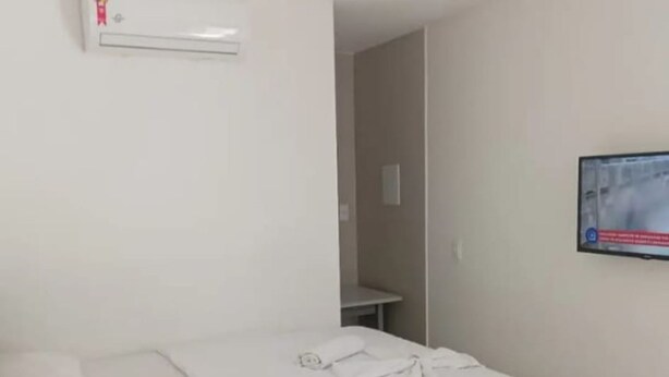 A hotel room with a bed, a TV mounted on the wall, and an air conditioning unit on the wall. - Pousada Brisa Suítes (Ipojuca)