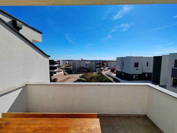 A balcony with a view of modern residential buildings, a wooden bench, and a clear blue sky.