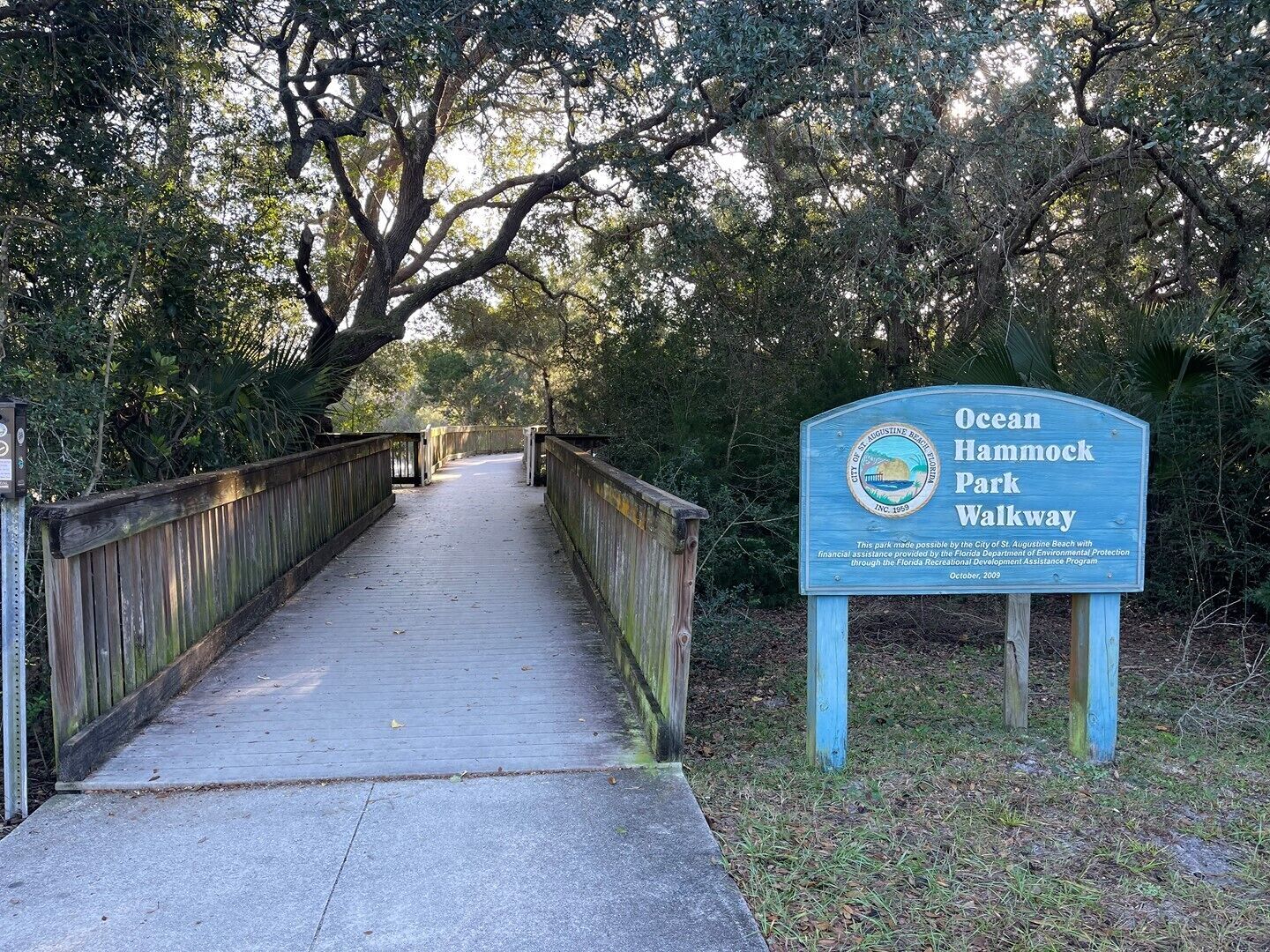 A wooden boardwalk leading through a wooded area with a sign for Ocean Hammock Park Walkway.
