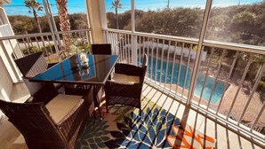 Ein Balkon mit Glastisch und Korbstühlen, mit Blick auf einen Pool und eine Wüstenlandschaft.