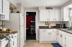 A modern kitchen with white cabinets, a microwave, and a red curtain in the background. - ⚓Sunset Getaways! Private Heated Pool home, Cinema/Arcade Room⚓ (Bradenton)