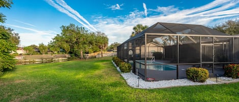 A modern house with a large glass-enclosed pool area, surrounded by a well-maintained lawn and trees.