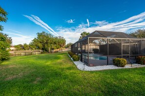 Une maison moderne dotée d’un grand espace piscine entièrement vitré, entourée d’une pelouse bien entretenue et d’arbres.