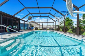A swimming pool with a basketball hoop, lounge chairs, and a covered area.