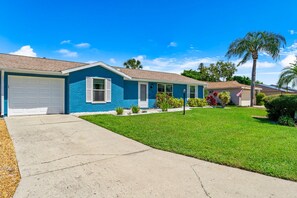 A residential house with a blue exterior, a front garage, and a well-maintained lawn.