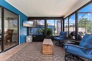 A sunroom with a view of the outdoors, a TV mounted on the wall, and a seating area with chairs and a table. - ⚓Sunset Getaways! Private Heated Pool home, Cinema/Arcade Room⚓ (Bradenton)