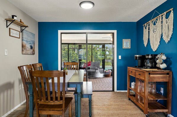 Un espace repas comprenant une table et des chaises, un coin café et une vue à travers une porte vitrée.